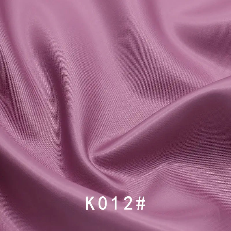 Gros plan sur un tissu satiné coloré en viscose au mètre de Longan Craft France, aux plis souples et portant la mention "K012#" en bas au centre - un élégant tissage sergé en polyester-viscose parfait pour les robes de cérémonie.