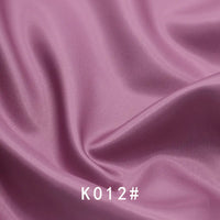 Gros plan sur un tissu satiné coloré en viscose au mètre de Longan Craft France, aux plis souples et portant la mention "K012#" en bas au centre - un élégant tissage sergé en polyester-viscose parfait pour les robes de cérémonie.