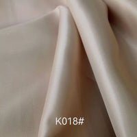 Gros plan sur le tissu viscose satiné beige clair de Longan Craft France, parfait pour les robes de cérémonie. Produit : Tissu satiné coloré en viscose au mètre (tissage sergé polyester-viscose). Code "K018#" visible en bas de l'image au centre.
