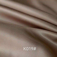 Gros plan sur le Tissu satiné coloré en viscose au mètre de Longan Craft France, lisse et marron clair, avec de légers plis. Le code "K019#" apparaît en blanc en bas au centre, mettant en valeur cette élégante étoffe idéale pour robes de cérémonie.
