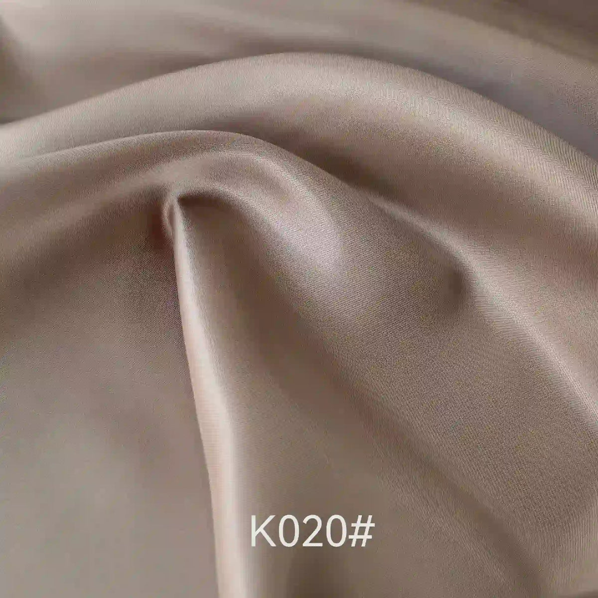 Gros plan sur le Tissu satiné coloré en viscose au mètre de Longan Craft France, montrant des plis lisses de couleur marron clair avec une brillance douce. Le texte "K020#" apparaît en bas. Idéal pour robes de cérémonie, alliant élégance et confort.