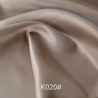 Gros plan sur le Tissu satiné coloré en viscose au mètre de Longan Craft France, montrant des plis lisses de couleur marron clair avec une brillance douce. Le texte "K020#" apparaît en bas. Idéal pour robes de cérémonie, alliant élégance et confort.