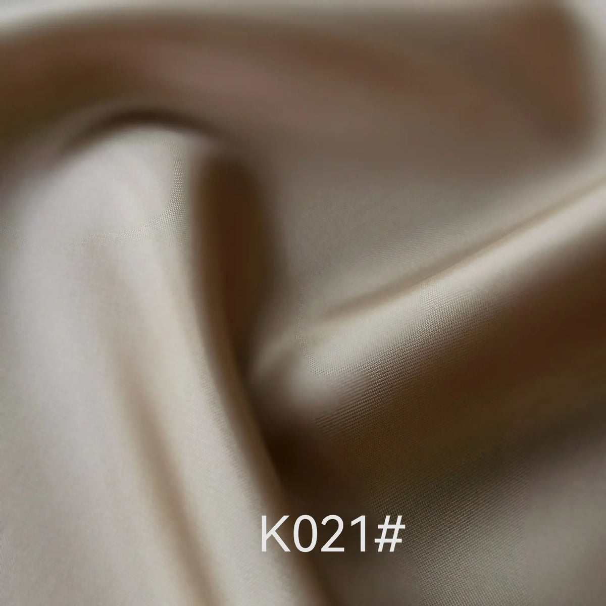 Gros plan sur un élégant tissu en satin de viscose beige de Longan Craft France, au lustre doux et aux plis subtils. Le code "K021#" est affiché en bas au centre. Parfait pour les robes d'occasions spéciales ; disponible au mètre.