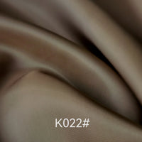 Gros plan sur le Tissu satiné coloré en viscose au mètre de Longan Craft France, montrant des plis souples et une texture visible. La mention "K022#" est affichée en blanc en bas au centre. Idéal pour les robes de cérémonie avec tissage sergé polyester-viscose.
