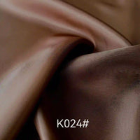 Un gros plan du tissu satiné coloré en viscose au mètre de Longan Craft France présente des plis et reflets lustrés. Le code K024# apparaît en bas au centre, illustrant cette élégante viscose idéale pour robes de cérémonie.