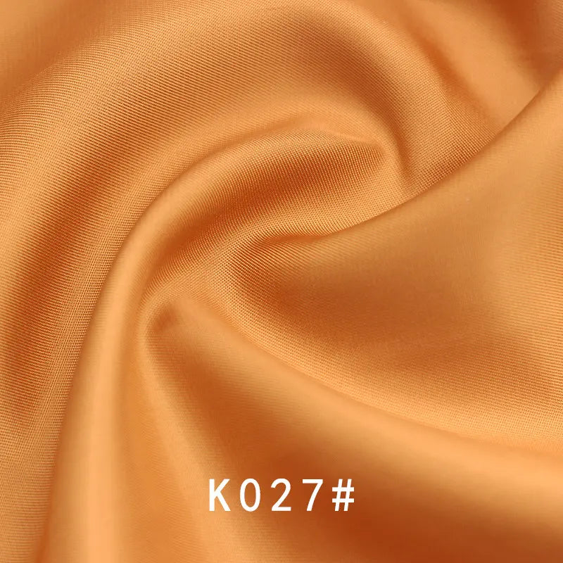 Gros plan sur le Tissu satiné coloré en viscose au mètre de Longan Craft France, aux plis élégants et à la brillance subtile. Idéal pour les robes de cérémonie. Le code "K027#" est indiqué en blanc au bas de l'image.