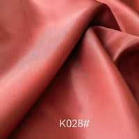 Gros plan sur le Tissu satiné coloré en viscose au mètre, lisse et brun rougeâtre, de Longan Craft France, montrant des plis doux et une légère brillance. Le texte "K028#" apparaît en bas au centre de l'image.
