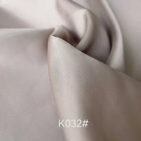 Gros plan sur le tissu satiné coloré en viscose au mètre de Longan Craft France, de couleur beige clair et lisse, à la texture douce et brillante et aux plis délicats. Idéal pour les robes de cérémonie. La mention "K032#" apparaît en bas au centre de l'image.