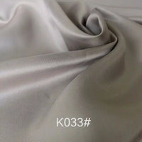 Gros plan sur un tissu satiné coloré en viscose au mètre, gris clair et lisse, de Longan Craft France, aux plis délicats et à l'éclat subtil. Le code "K033#" est superposé en texte blanc près du centre inférieur.