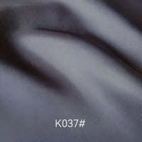 Élégant tissu satiné en viscose gris foncé plié de Longan Craft France, au tissage sergé et à la texture douce, parfait pour les robes de cérémonie. Le code "K037#" apparaît en blanc en bas au centre de l'image.