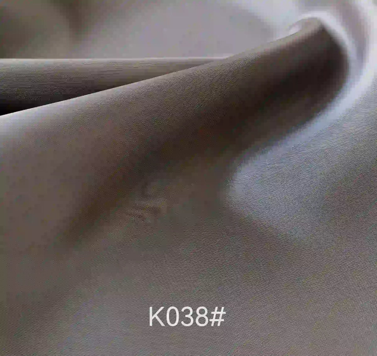 Gros plan sur le tissu satiné coloré en viscose au mètre de Longan Craft France, aux plis doux et à la texture moelleuse. Tissage sergé polyester-viscose, élégant pour les robes de cérémonie. Code "K038#" en bas au centre.