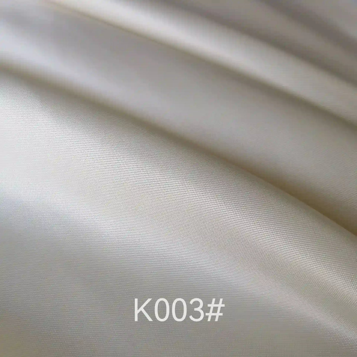 Gros plan sur un tissu satiné coloré en viscose de Longan Craft France, de couleur ivoire clair et lisse, aux plis délicats et à la texture douce et soyeuse. La mention "K003#" apparaît en bas au centre. Idéal pour les robes de cérémonie élégantes.