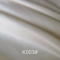 Gros plan sur un tissu satiné coloré en viscose de Longan Craft France, de couleur ivoire clair et lisse, aux plis délicats et à la texture douce et soyeuse. La mention "K003#" apparaît en bas au centre. Idéal pour les robes de cérémonie élégantes.