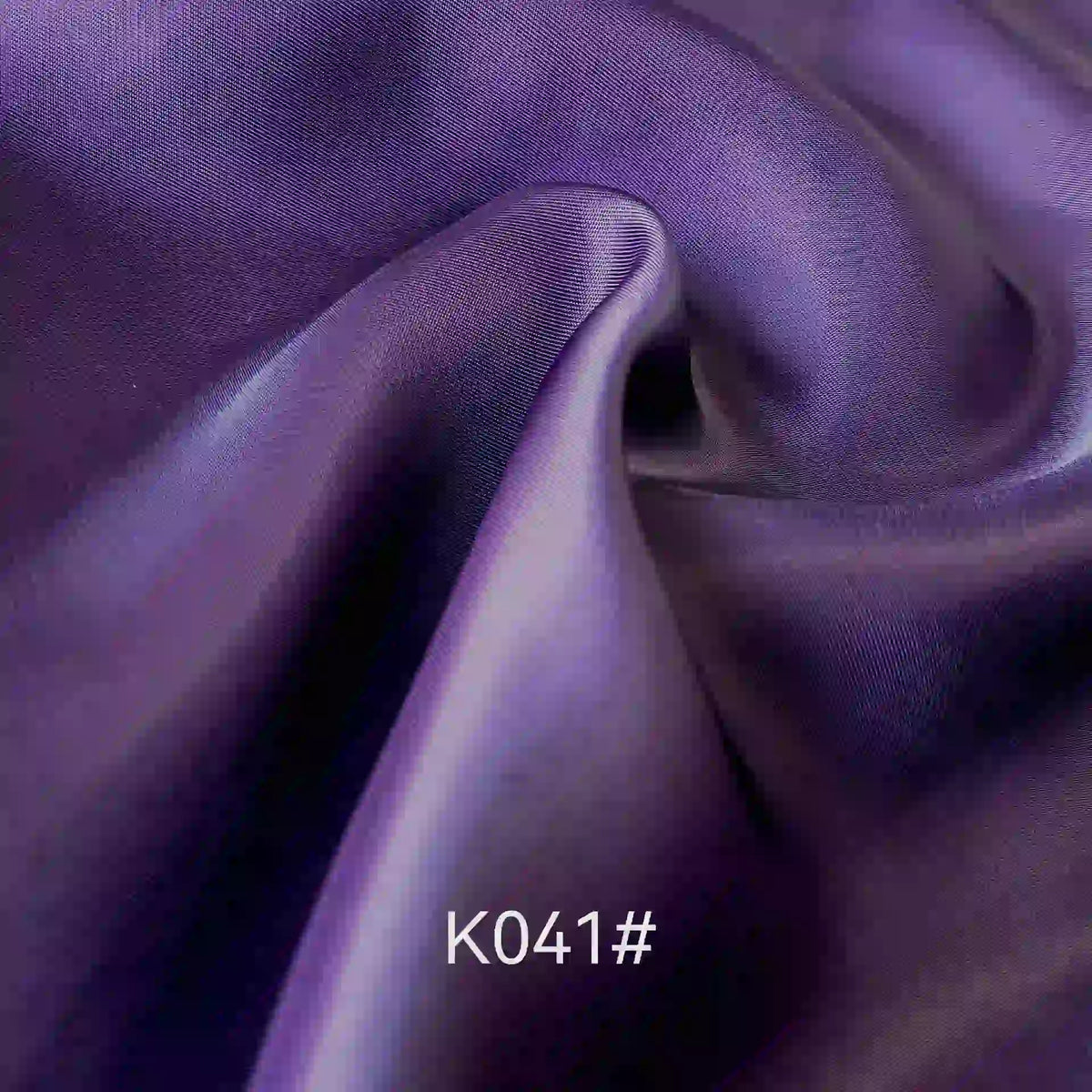 Gros plan sur le tissu satiné coloré en viscose au mètre, tissage sergé polyester-viscose de Longan Craft France. La texture soyeuse et élégante avec des plis est parfaite pour les robes de cérémonie. Le code "K041#" apparaît en bas au centre.