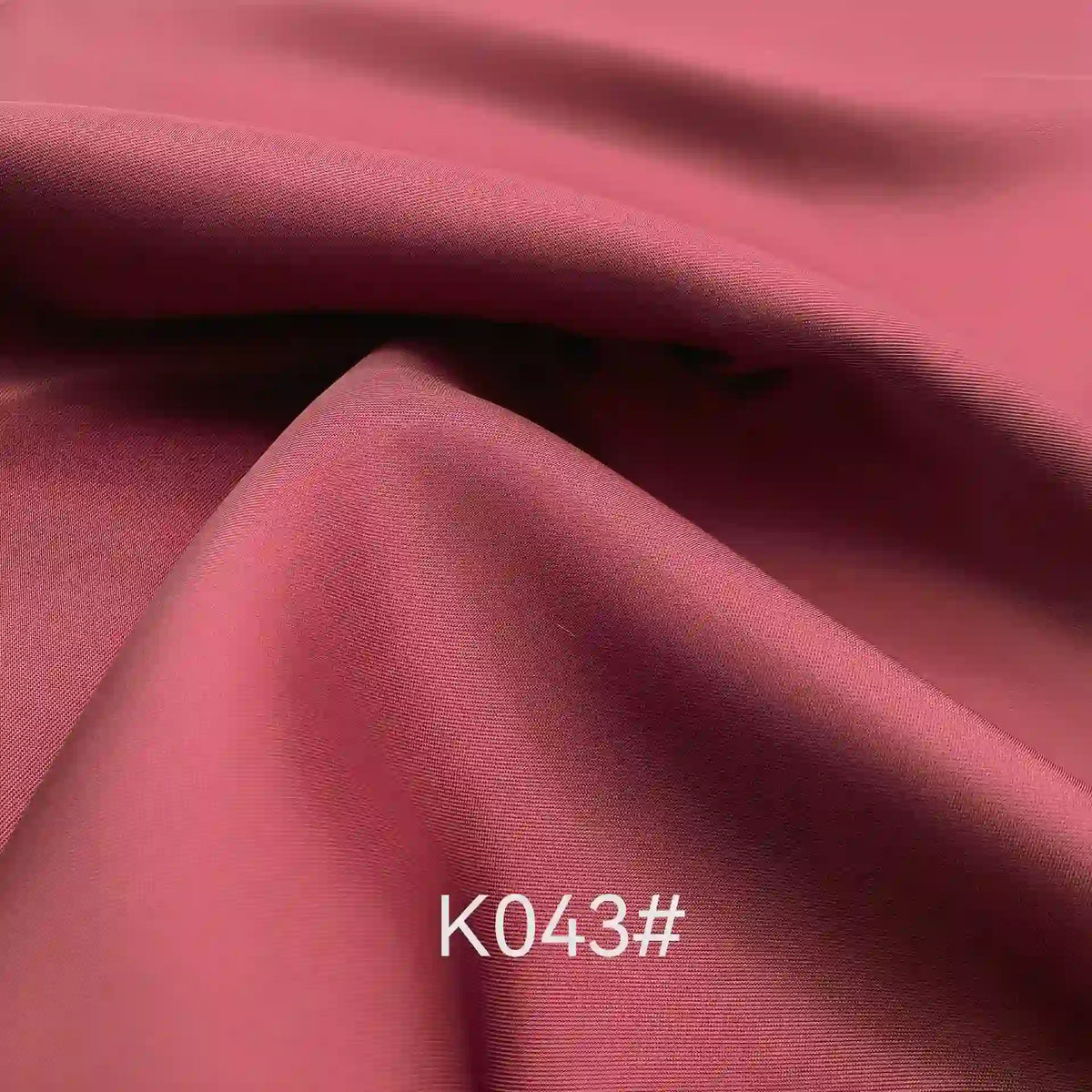 Gros plan sur le pliage du Tissu satiné coloré en viscose au mètre de Longan Craft France, mettant en valeur sa texture lisse et légèrement brillante en polyester sergé-viscose - élégante et idéale pour les robes de cérémonie. Le code "K043#" apparaît en blanc en bas.