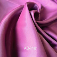 Gros plan sur le Tissu satiné coloré en viscose au mètre de Longan Craft France en violet, montrant des plis doux et une brillance subtile. Idéal pour robes de cérémonie et créations élégantes, tissage sergé polyester-viscose.