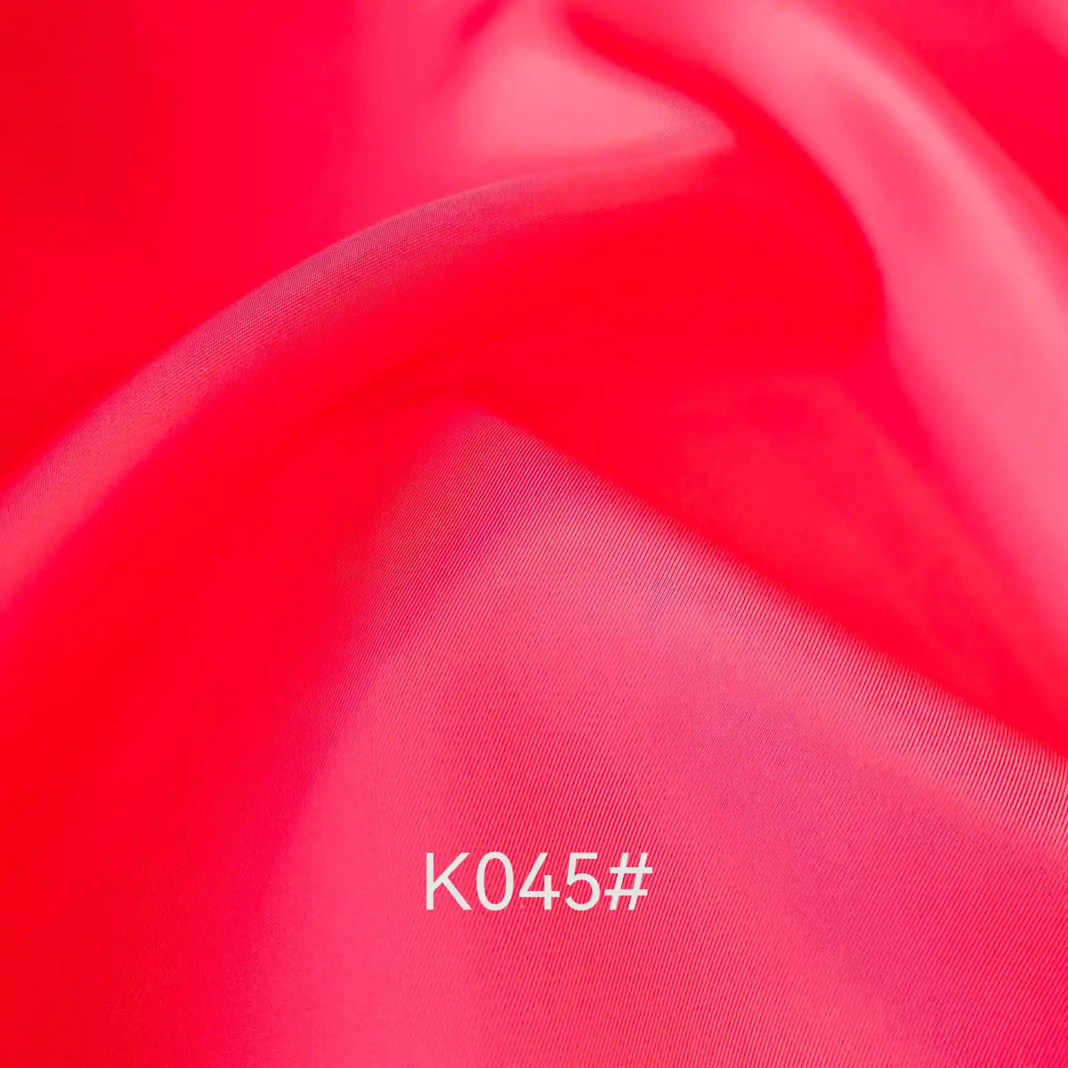 Gros plan sur un Tissu satiné coloré en viscose au mètre, rose vif et lisse, de Longan Craft France, présentant de légers plis et le code "K045#" en blanc près du centre. Cet élégant polyester-viscose sergé est idéal pour les robes de cérémonie.