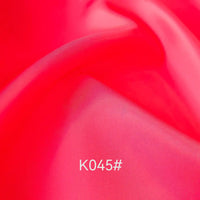 Gros plan sur un Tissu satiné coloré en viscose au mètre, rose vif et lisse, de Longan Craft France, présentant de légers plis et le code "K045#" en blanc près du centre. Cet élégant polyester-viscose sergé est idéal pour les robes de cérémonie.