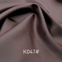Gros plan sur le tissu satiné coloré en viscose au mètre, tissage sergé polyester-viscose de Longan Craft France, drapé en plis souples avec "K047#" superposé sur la partie inférieure - idéal pour les robes de cérémonie élégantes.