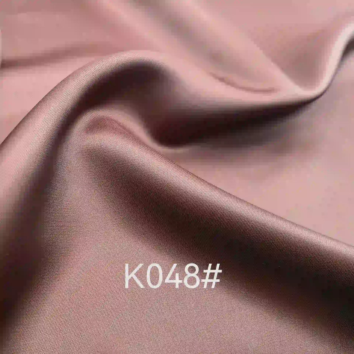 Tissu satiné viscose rose-brun lisse et brillant de Longan Craft France, idéal pour les robes de cérémonie. Tissage sergé polyester-viscose avec plis doux et code "K048#" imprimé en bas au centre.