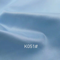 Un gros plan du Tissu satiné coloré en viscose au mètre de Longan Craft France montre sa texture lisse en polyester-viscose sergé bleu clair avec de légers plis. L'étiquette "K051#" apparaît en blanc au centre de l'image.