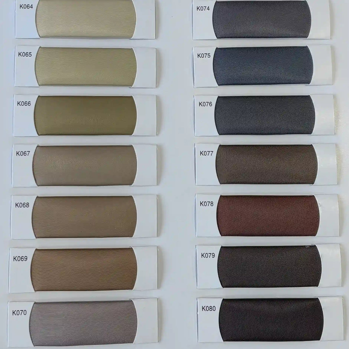 Douze échantillons rectangulaires de tissu satiné coloré en viscose Longan Craft France, numérotés K064-K080, présentent une gamme de tons élégants, parfaits pour des robes de cérémonie. Tissage sergé polyester-viscose.