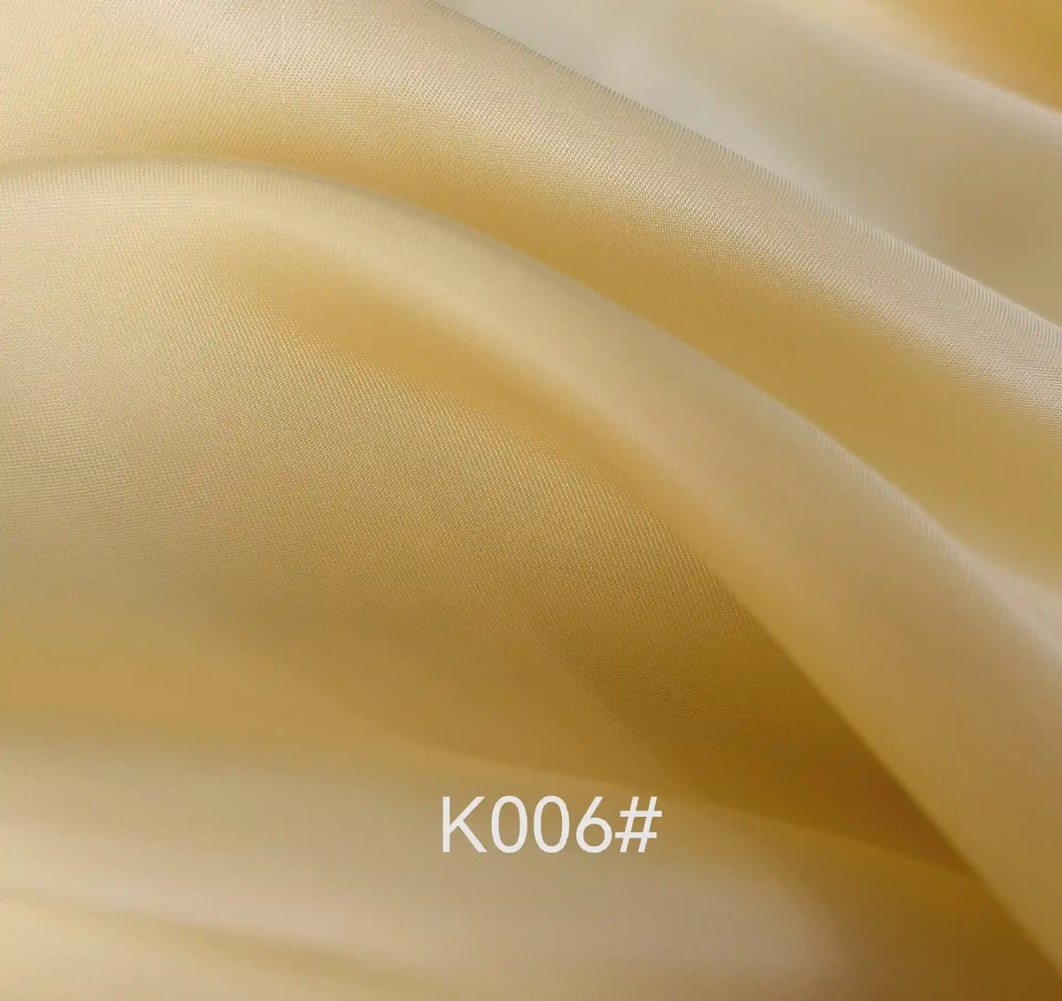 Gros plan sur un tissu satiné viscose jaune clair, lisse, aux plis délicats et à la brillance subtile. La mention "K006#" apparaît en bas. Produit : Tissu satiné coloré polyester-viscose par Longan Craft France, idéal pour les robes élégantes.