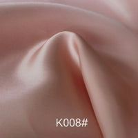 Gros plan sur le Tissu satiné coloré en viscose au mètre de Longan Craft France, rose pâle, lisse et légèrement brillant, présentant de légers plis et la mention "K008#" incrustée en bas au centre. Idéal pour les robes de cérémonie au tissage sergé polyester-viscose.