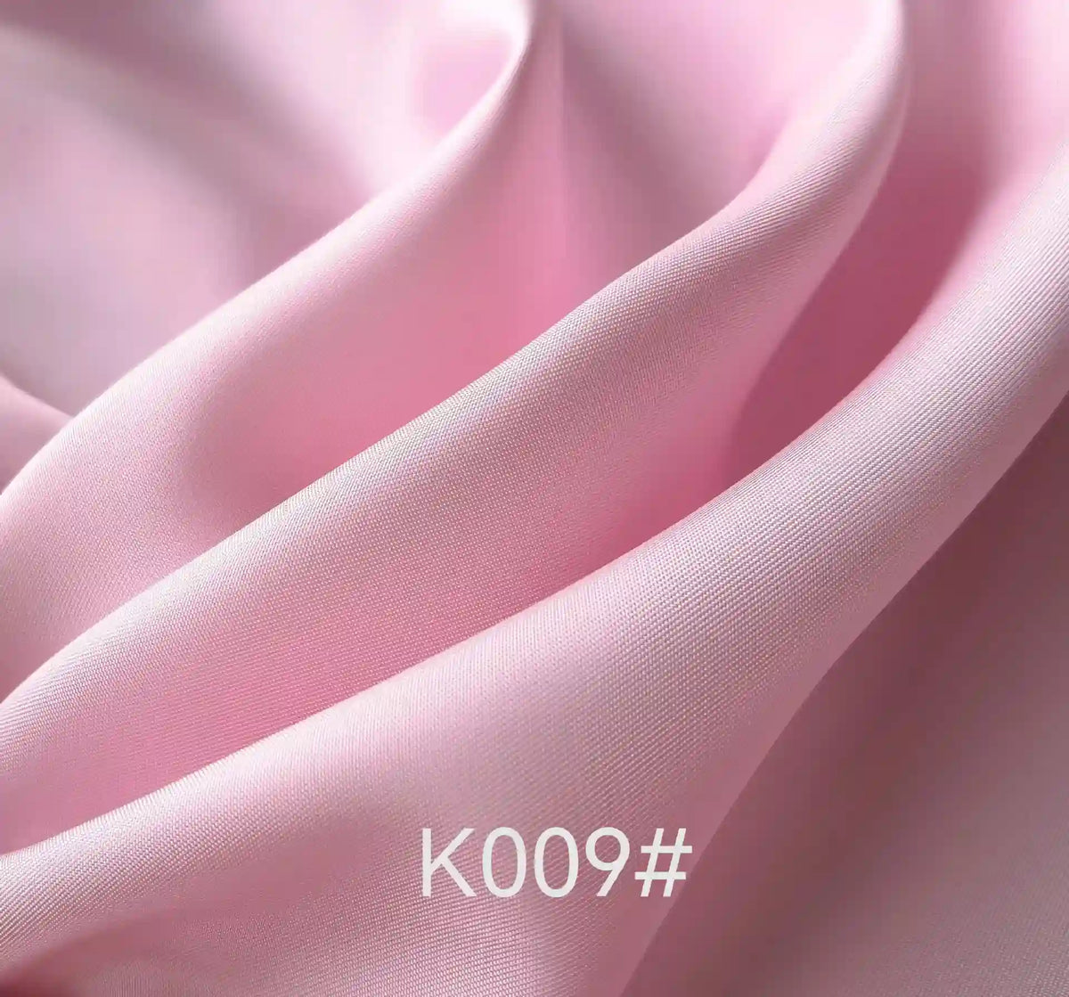 Gros plan sur le "Tissu satiné coloré en viscose au mètre" de Longan Craft France, un tissu doux et brillant en viscose-polyester rose pâle aux plis lisses. Le code produit "K009#" apparaît en texte blanc en bas au centre.