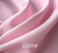 Gros plan sur le "Tissu satiné coloré en viscose au mètre" de Longan Craft France, un tissu doux et brillant en viscose-polyester rose pâle aux plis lisses. Le code produit "K009#" apparaît en texte blanc en bas au centre.