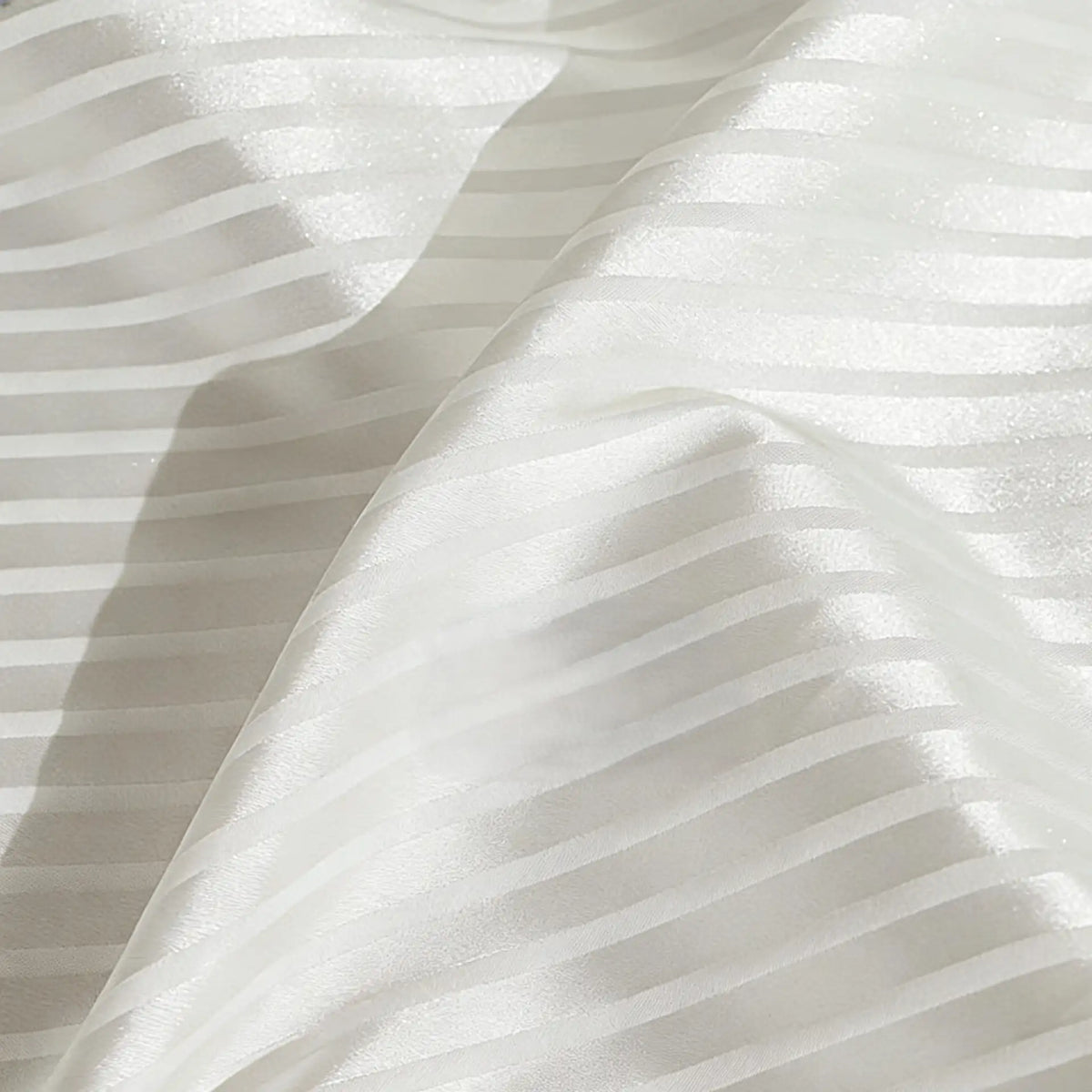 Gros plan sur le Tissu satiné jacquard rayé coloré au mètre de Longan Craft France, montrant des bandes horizontales brillantes et mates. Ce tissu satiné en polyester, légèrement plié, est idéal pour la confection de robes élégantes.