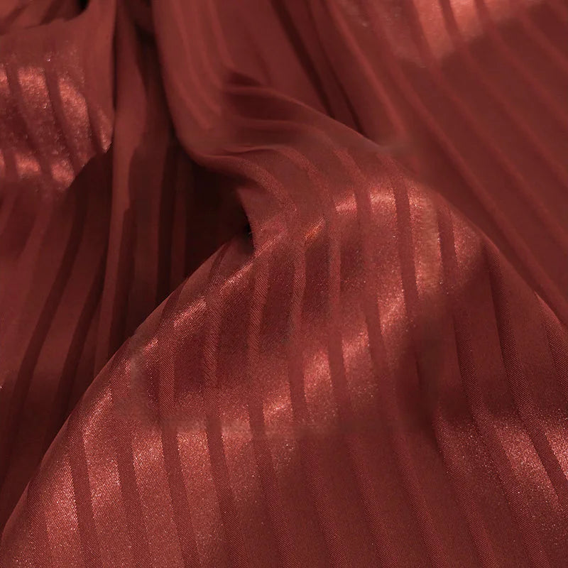 Gros plan sur le Tissu satin jacquard rayé coloré au mètre de Longan Craft France, un tissu satiné brillant avec des rayures verticales transparentes et opaques, doucement drapé avec des plis doux - idéal matière satinée pour confection de robes.