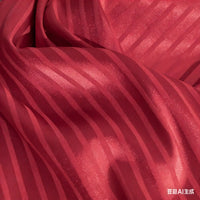 Un gros plan du Tissu satin jacquard rayé coloré au mètre de Longan Craft France montre sa texture brillante et ondulée avec des rayures verticales et des plis souples - un satin idéal pour la confection de robes.