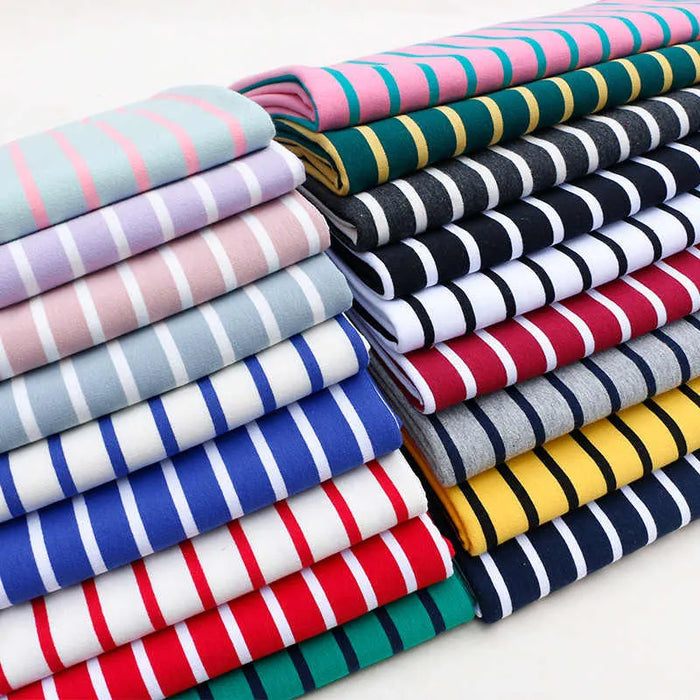 Une pile colorée de tissu French Terry extensible rayé de Longan Craft France, disponible au mètre en bleu, rouge, jaune, vert, rose, gris, blanc et noir - le tricot de coton idéal pour les sweatshirts avec de douces rayures horizontales.