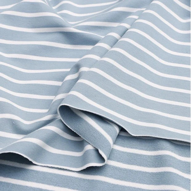 Un gros plan du Tissu French Terry extensible rayé coloré au mètre de Longan Craft France montre son tissu bleu clair avec des rayures blanches horizontales, délicatement plié pour révéler la douceur de la maille de coton - idéal pour la fabrication de sweatshirts.