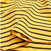 Un gros plan du Tissu French Terry extensible rayé coloré au mètre de Longan Craft France montre un tricot de coton jaune avec des rayures noires, légèrement plié et lisse - idéal pour les sweat-shirts.