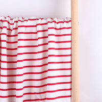 Un rideau blanc à rayures rouges horizontales en Tissu French Terry extensible rayé coloré de Longan Craft France est suspendu à une tringle en bois clair contre un mur blanc uni.