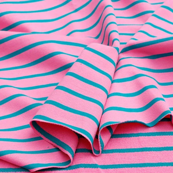 Le tissu French Terry extensible rayé coloré de Longan Craft France, en coton tricoté idéal pour sweatshirts, présente des rayures turquoise régulières sur fond rose, drapé et légèrement plié.