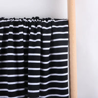 Le French Terry extensible rayé coloré au mètre de Longan Craft France, un tricot de coton idéal pour les sweat-shirts, est présenté en noir avec des rayures horizontales blanches, drapé sur une tige en bois clair sur un fond blanc uni.