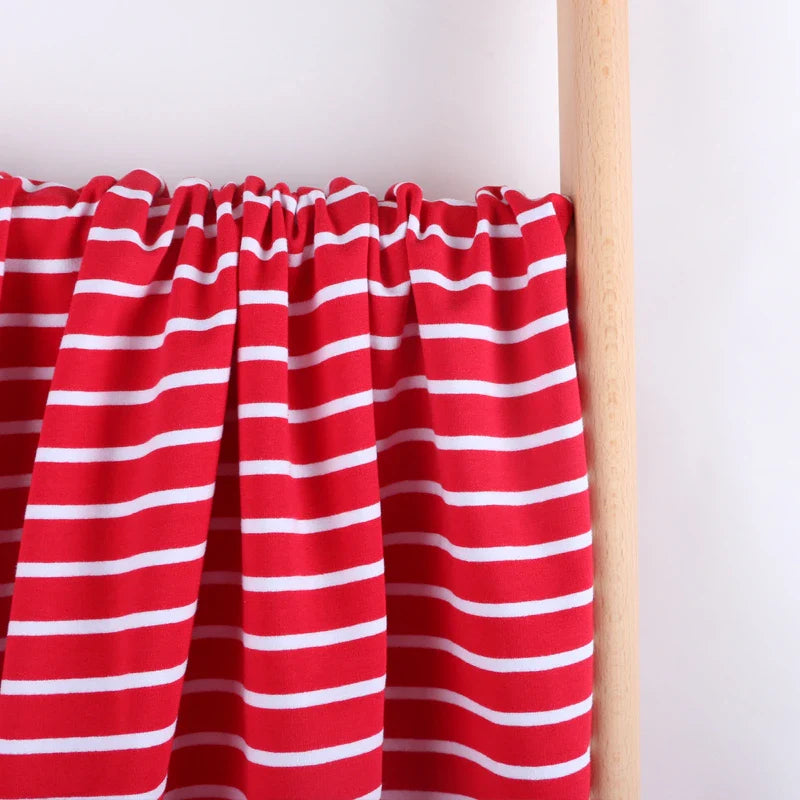 Un morceau de Tissu French Terry extensible rayé coloré au mètre de Longan Craft France, présentant des rayures blanches horizontales régulièrement espacées, est drapé sur une tige en bois sur un fond blanc uni.