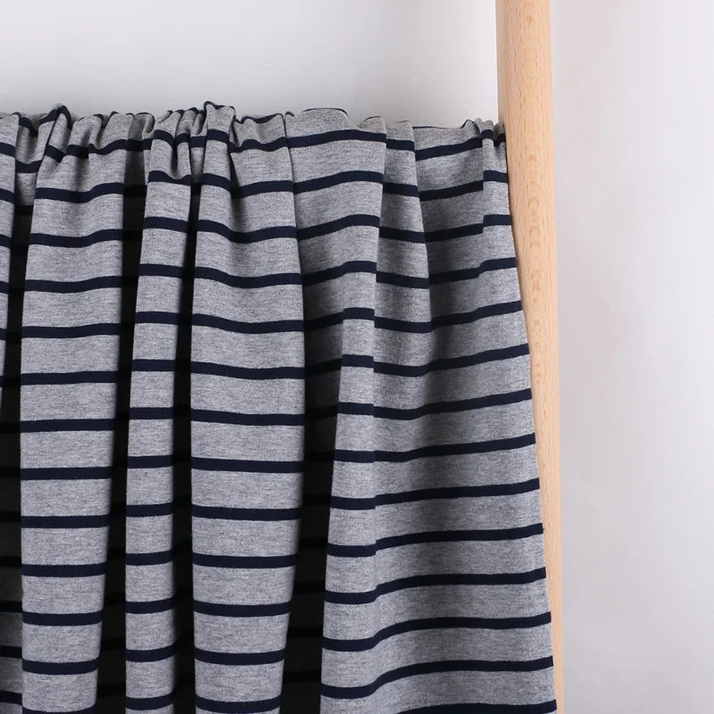 Le tissu French Terry extensible rayé coloré de Longan Craft France, idéal pour sweatshirts, est présenté suspendu sur une tringle en bois devant un fond blanc épuré.