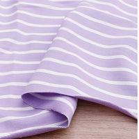 Gros plan sur le Tissu French Terry extensible rayé coloré de Longan Craft France, en coton tricoté lilas à rayures blanches, légèrement plié et posé sur une surface en bois. Idéal pour sweatshirts.