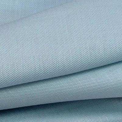Gros plan sur le tissu lyocell sergé au mètre bleu clair de Longan Craft France, un tissu 100% lyocell durable avec une texture subtile de côtes diagonales, présenté en plis nets et superposés - parfait pour des costumes confortables.
