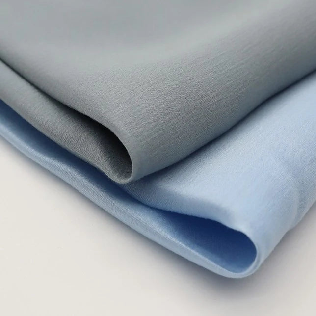 Deux pièces du tissu viscose challis de Longan Craft France, un mélange léger de viscose et de polyester pour les chemises protégeant du soleil, dans des tons doux et multicolores, sont présentées pliées avec une texture lisse et une brillance subtile.