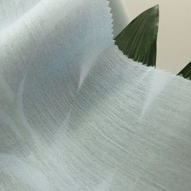 Gros plan sur Tissu en viscose challis multicolore au mètre de Longan Craft France, un tissu léger et respirant en viscose-polyester au motif subtil et à la texture douce, drapé sur des feuilles vertes pour des chemises protégeant du soleil.