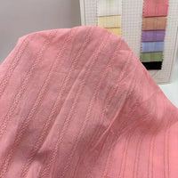 Au premier plan, un tissu ratière en viscose rose de Longan Craft France, idéal pour les robes de bricolage, est drapé. Derrière, une carte d'échantillons montre des échantillons du mélange coton et rayonne jacquard disponible au mètre dans différentes couleurs.