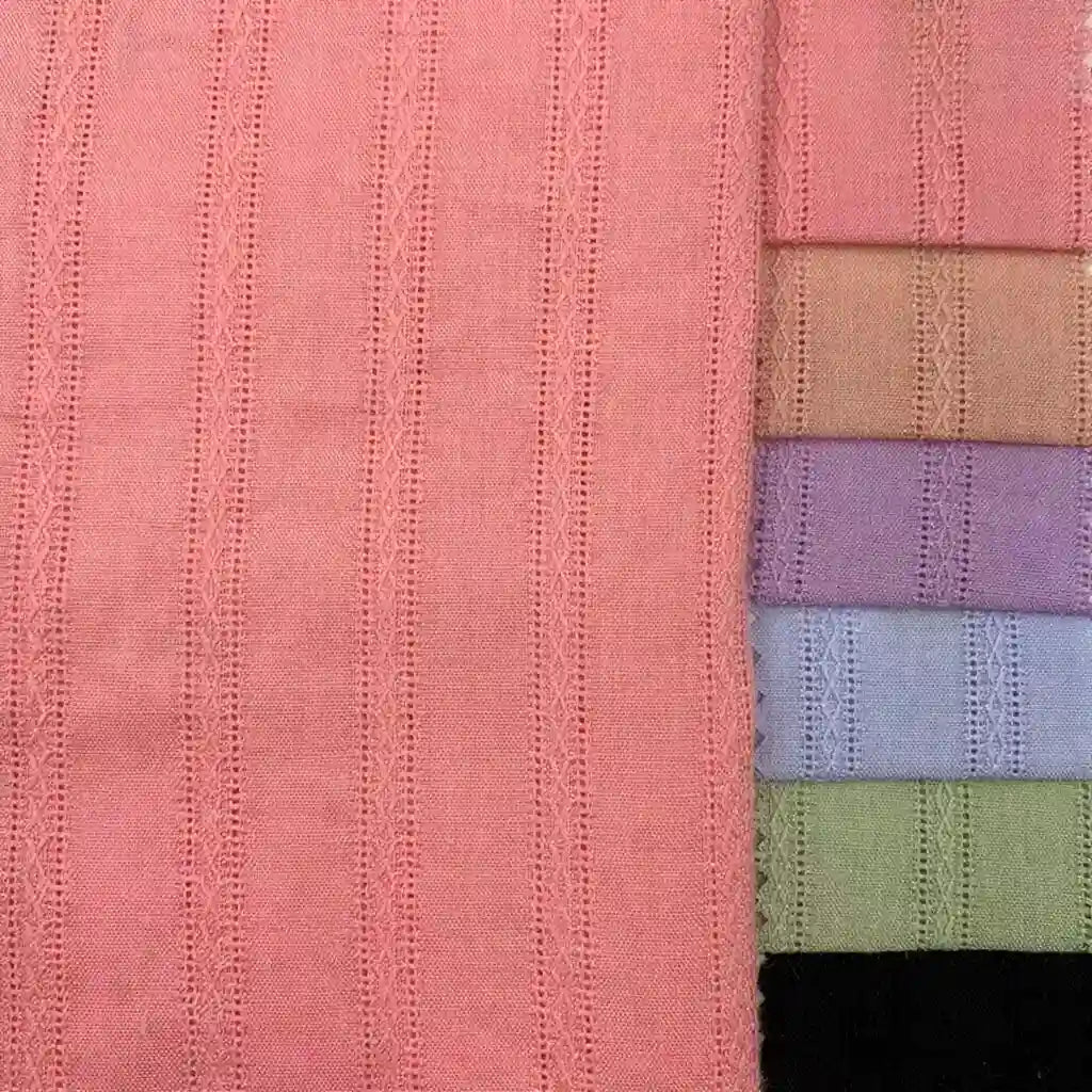 Sept pièces pliées du tissu dobby en viscose colorée (mélange coton et rayonne jacquard) de Longan Craft France sont disposées verticalement à côté d'un tissu rose plus grand avec un motif vertical cousu, idéal pour les peignoirs DIY.
