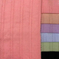 Sept pièces pliées du tissu dobby en viscose colorée (mélange coton et rayonne jacquard) de Longan Craft France sont disposées verticalement à côté d'un tissu rose plus grand avec un motif vertical cousu, idéal pour les peignoirs DIY.