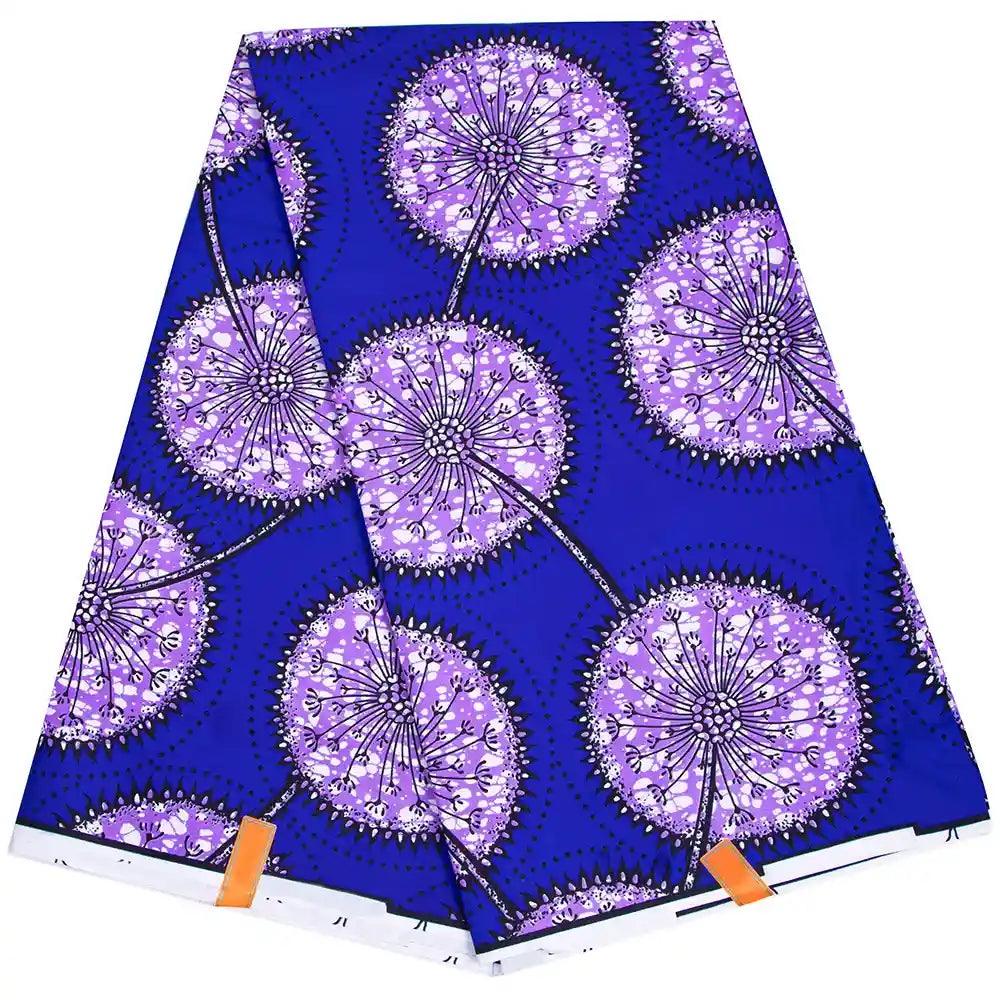 Un morceau plié de tissu wax africain Ankara coloré de Longan Craft France présente un fond bleu vif avec de grandes fleurs de pissenlit stylisées, des tiges noires, des accents blancs et deux étiquettes orange visibles sur le bord.