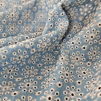 Gros plan sur le tissu de coton bleu clair de Longan Craft France, "Tissu jean brodé floral ajouré", montrant des motifs floraux brodés aériens et des plis doux dans le tissu 100 % coton.